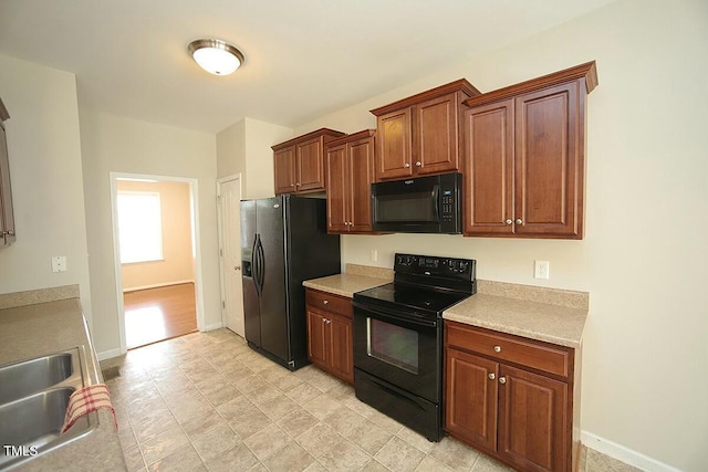 kitchen featuring baseboards, a sink, light countertops, and black appliances