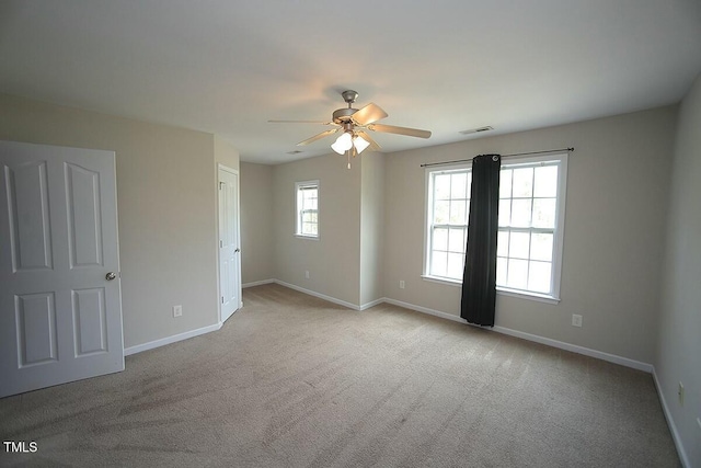 carpeted spare room with visible vents, baseboards, and a ceiling fan