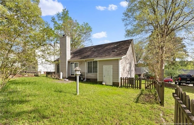 rear view of property featuring a yard, fence, and a chimney