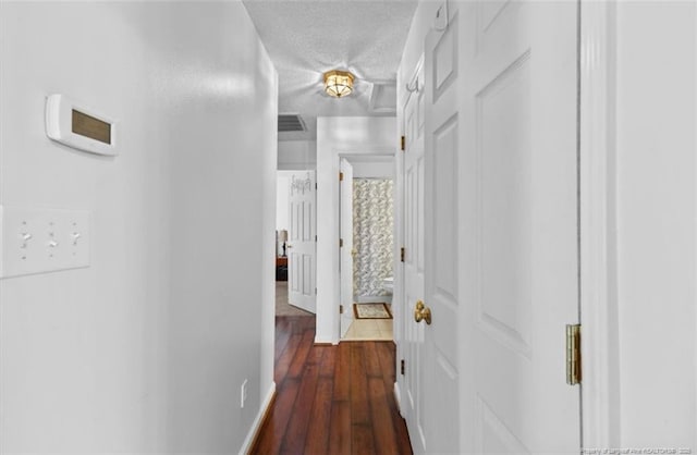 corridor featuring visible vents, baseboards, wood finished floors, and a textured ceiling