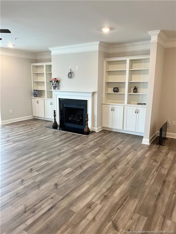 unfurnished living room with crown molding, wood finished floors, a fireplace, and baseboards