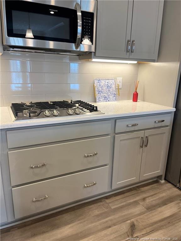 kitchen with gray cabinets, light wood-type flooring, appliances with stainless steel finishes, and decorative backsplash