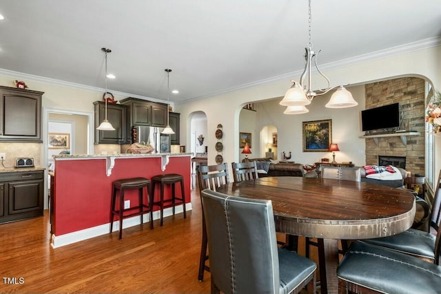 12808 Edsel Dr, Raleigh, NC 27613 - dining area with arched walkways, ornamental molding, a stone fireplace, recessed lighting, and dark wood-style floors