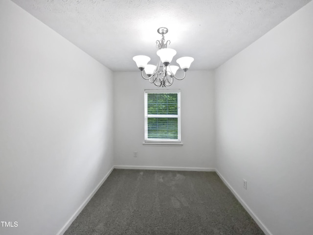 spare room featuring a chandelier, a textured ceiling, dark colored carpet, and baseboards