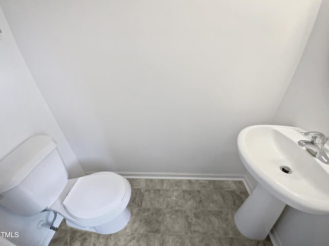 half bathroom with toilet, a sink, and baseboards