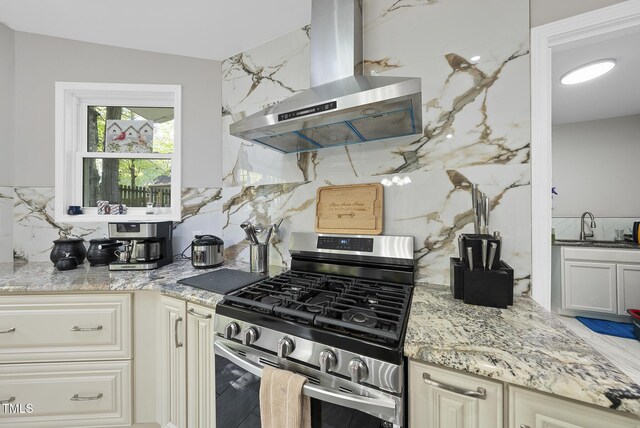 kitchen featuring tasteful backsplash, stainless steel range with gas cooktop, light stone countertops, island range hood, and a sink