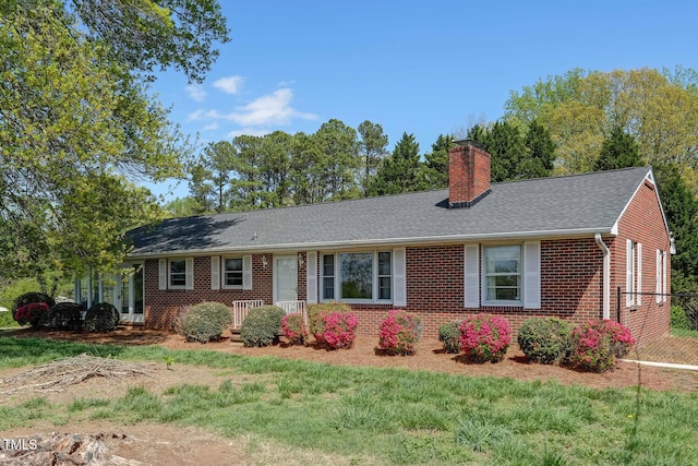 ranch-style house featuring roof with shingles, brick siding, a chimney, and a front yard