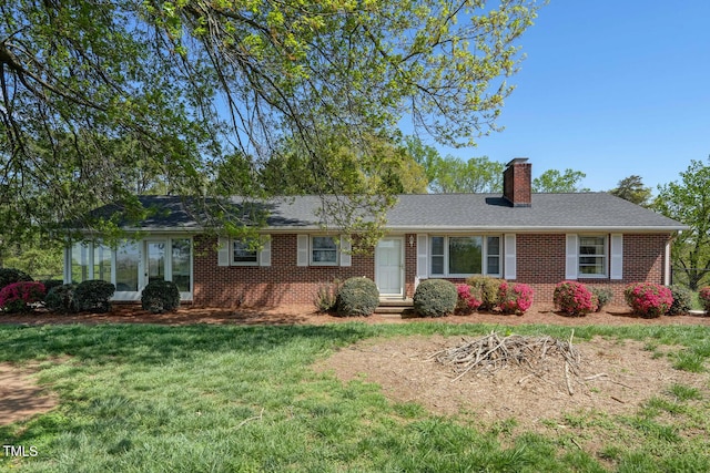 single story home featuring brick siding, a chimney, a sunroom, and a front lawn