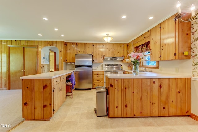 kitchen with a peninsula, ornamental molding, appliances with stainless steel finishes, under cabinet range hood, and light countertops