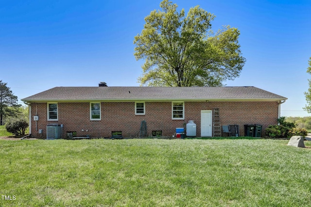 rear view of house with brick siding, cooling unit, a yard, and a chimney