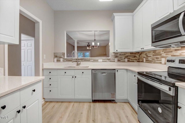 kitchen with an inviting chandelier, a sink, appliances with stainless steel finishes, light wood finished floors, and decorative backsplash