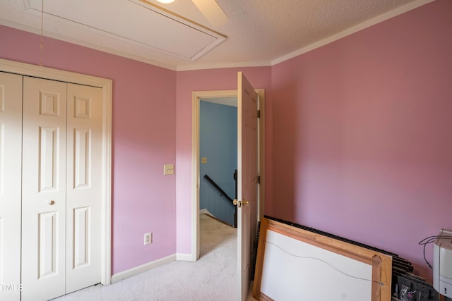 unfurnished bedroom featuring a closet, baseboards, a textured ceiling, attic access, and light carpet