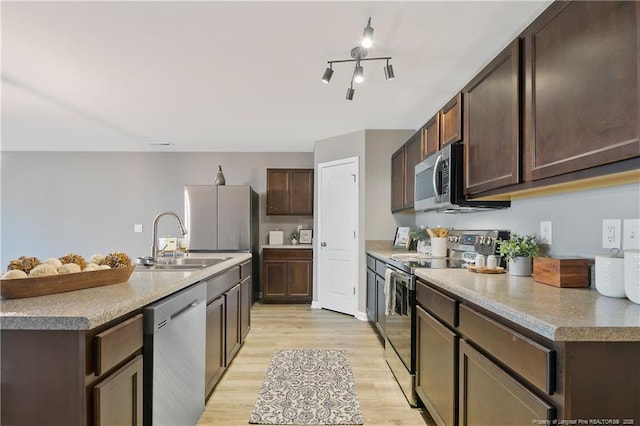 kitchen featuring light wood-style floors, dark brown cabinets, a sink, stainless steel appliances, and a center island with sink
