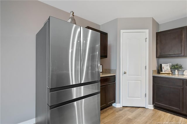 kitchen featuring light wood-style flooring, freestanding refrigerator, dark brown cabinetry, and baseboards