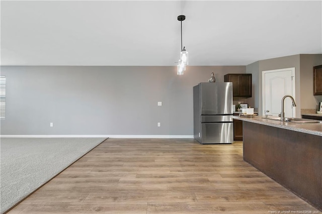 kitchen featuring baseboards, decorative light fixtures, a sink, freestanding refrigerator, and dark brown cabinetry