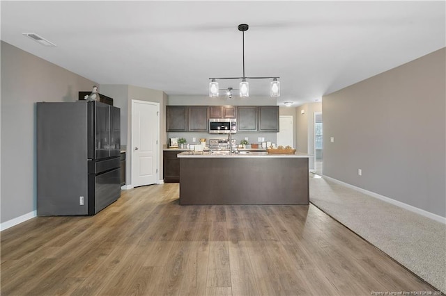 kitchen featuring visible vents, baseboards, freestanding refrigerator, dark brown cabinetry, and stainless steel microwave