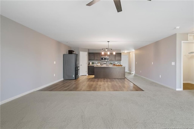 kitchen with freestanding refrigerator, a ceiling fan, stainless steel microwave, open floor plan, and baseboards