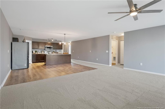 unfurnished living room with light carpet, baseboards, and a ceiling fan