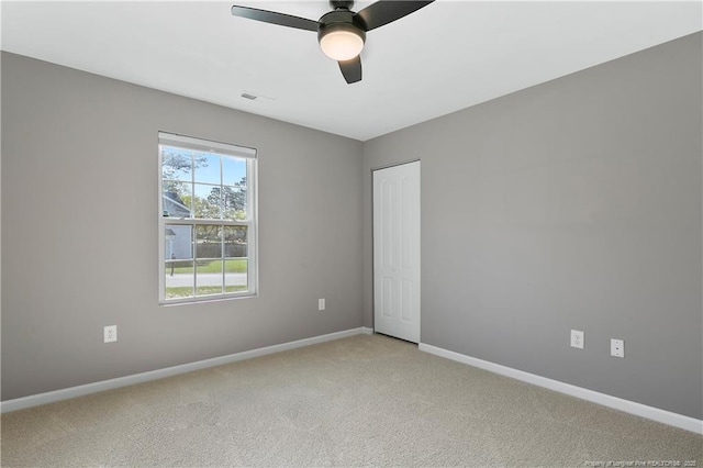 empty room featuring light carpet, visible vents, baseboards, and a ceiling fan