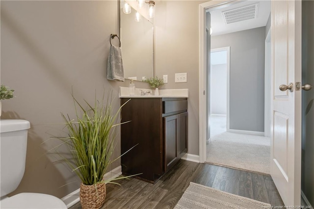 half bathroom featuring vanity, visible vents, toilet, wood finished floors, and baseboards