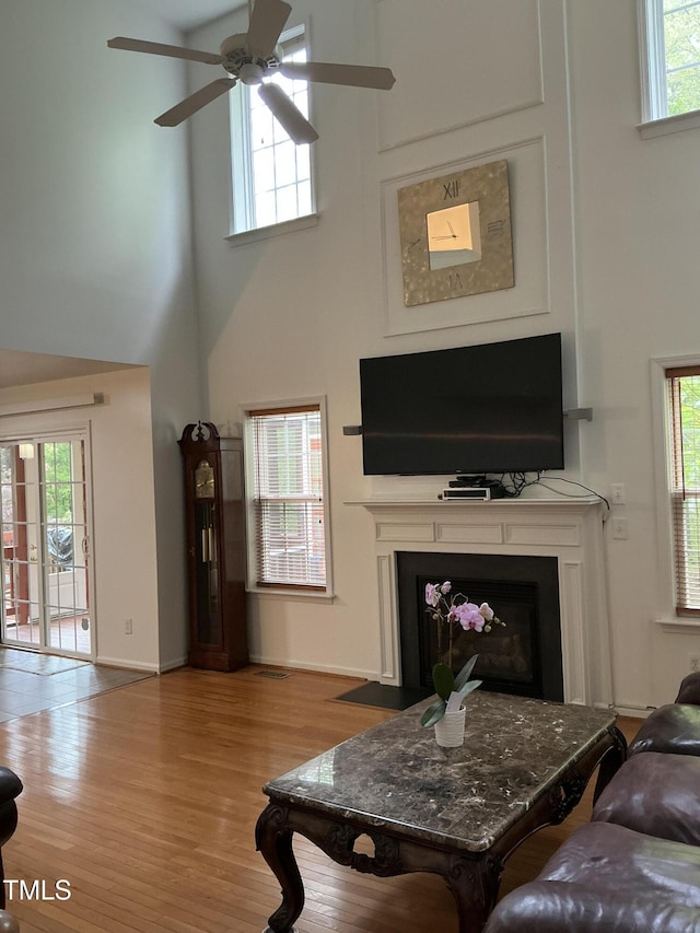 living area with ceiling fan, a fireplace, a towering ceiling, wood finished floors, and baseboards