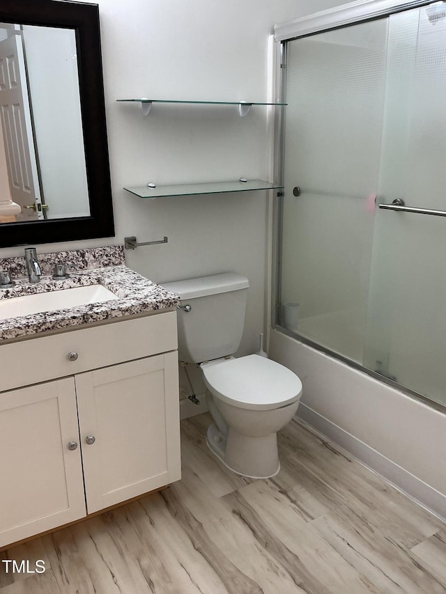 bathroom with toilet, vanity, wood finished floors, and bath / shower combo with glass door