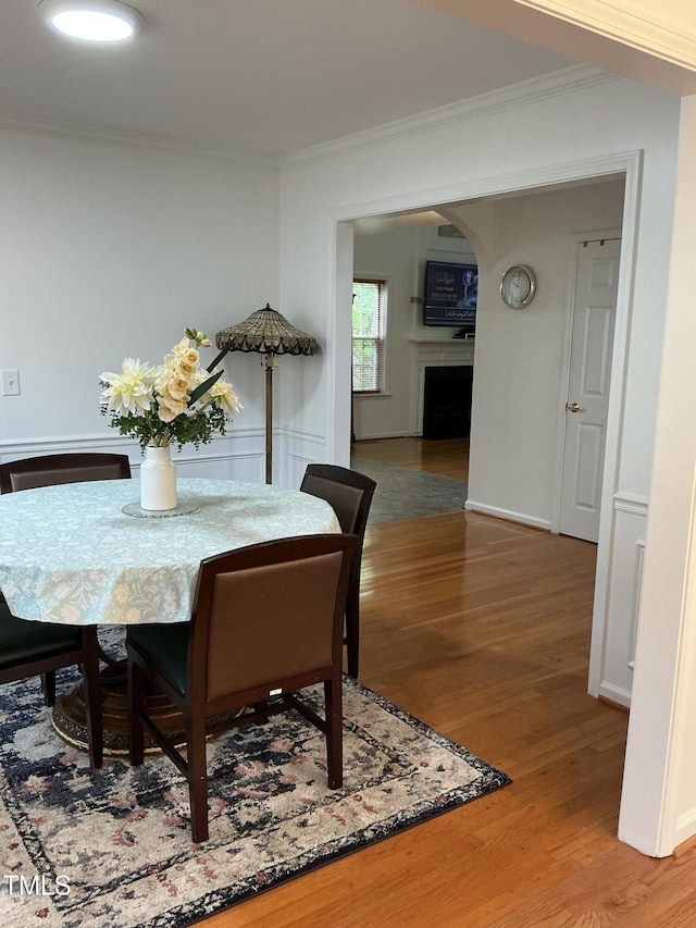 dining room featuring crown molding, light wood-style flooring, arched walkways, and a fireplace
