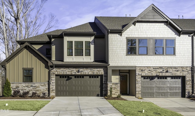 craftsman inspired home with a shingled roof, stone siding, a garage, board and batten siding, and concrete driveway
