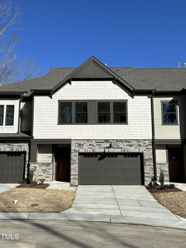 view of front of home featuring driveway, stone siding, a garage, and roof with shingles