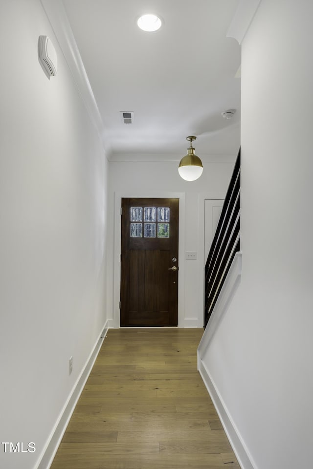 foyer entrance featuring light wood-style flooring, ornamental molding, visible vents, stairs, and baseboards