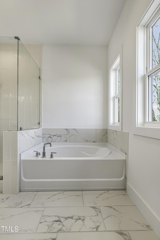 bathroom with plenty of natural light, a bath, and marble finish floor