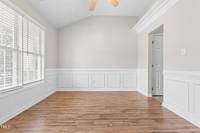 empty room featuring light wood-type flooring, a wainscoted wall, a ceiling fan, and a healthy amount of sunlight
