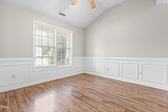 empty room with light wood finished floors, a ceiling fan, vaulted ceiling, and a wainscoted wall