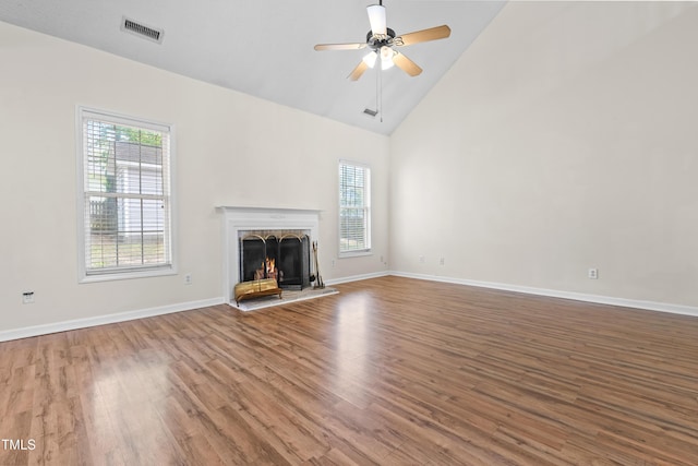 unfurnished living room with visible vents, a warm lit fireplace, ceiling fan, wood finished floors, and high vaulted ceiling