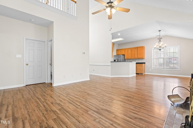unfurnished living room featuring light wood-type flooring, ceiling fan with notable chandelier, high vaulted ceiling, and baseboards