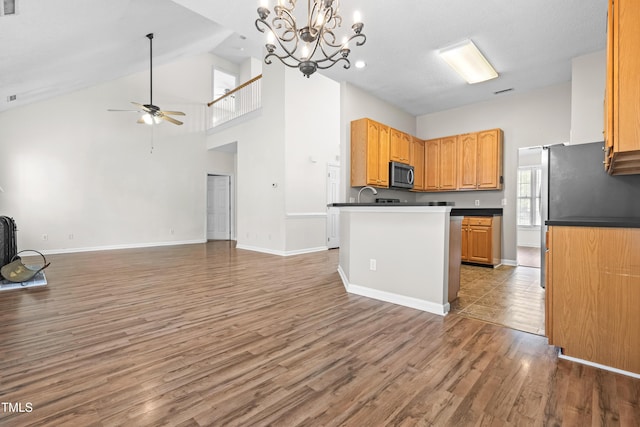 kitchen with ceiling fan with notable chandelier, high vaulted ceiling, wood finished floors, dark countertops, and open floor plan