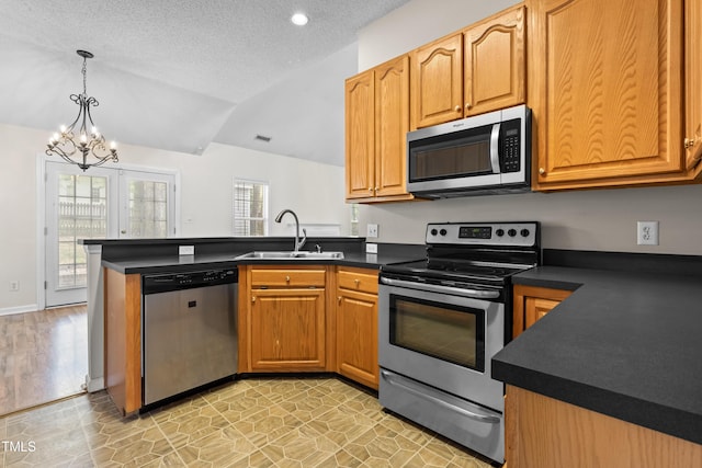 kitchen with an inviting chandelier, a sink, appliances with stainless steel finishes, dark countertops, and a peninsula