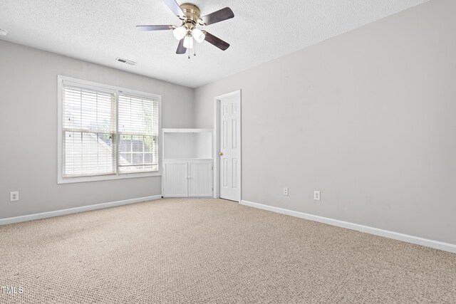 empty room with visible vents, a textured ceiling, light colored carpet, and a ceiling fan