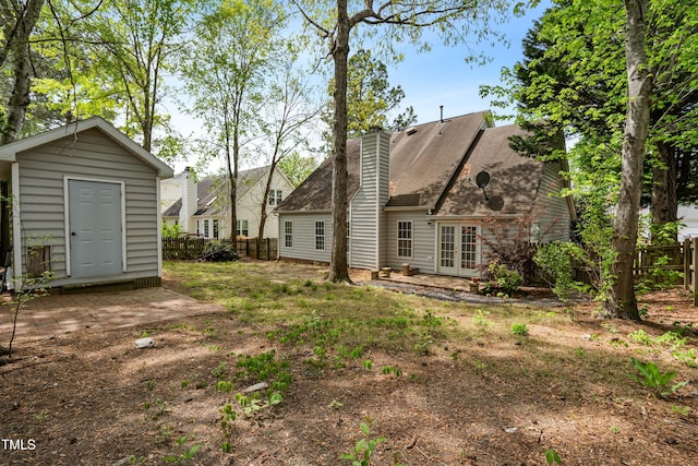 rear view of house featuring a chimney, french doors, a shed, an outbuilding, and fence