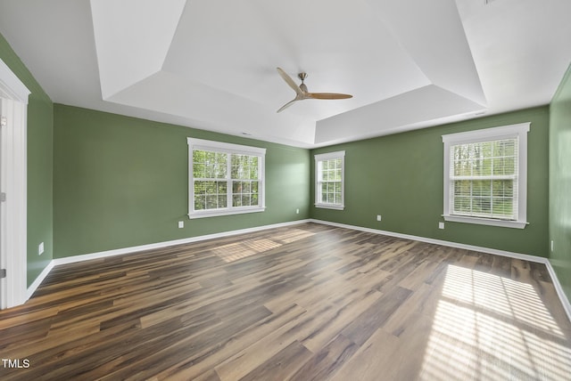 unfurnished room with a tray ceiling, wood finished floors, ceiling fan, and baseboards