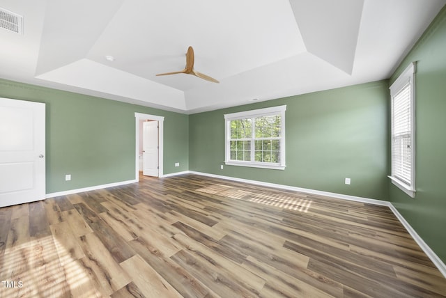 unfurnished room with baseboards, visible vents, a tray ceiling, ceiling fan, and wood finished floors