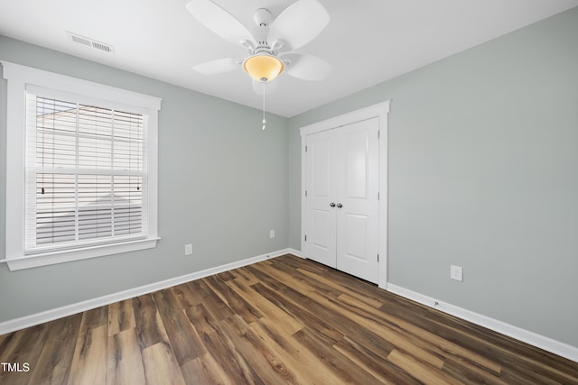 empty room with visible vents, baseboards, a ceiling fan, and dark wood finished floors