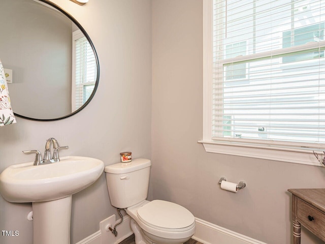 bathroom with baseboards, healthy amount of natural light, toilet, and a sink