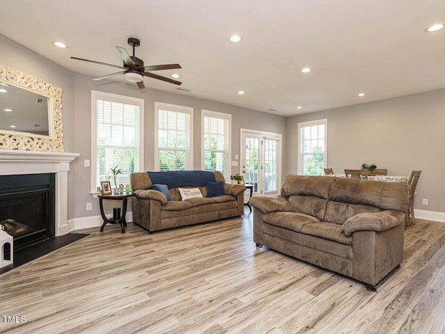 living area with light wood-type flooring, recessed lighting, a ceiling fan, baseboards, and a fireplace with flush hearth