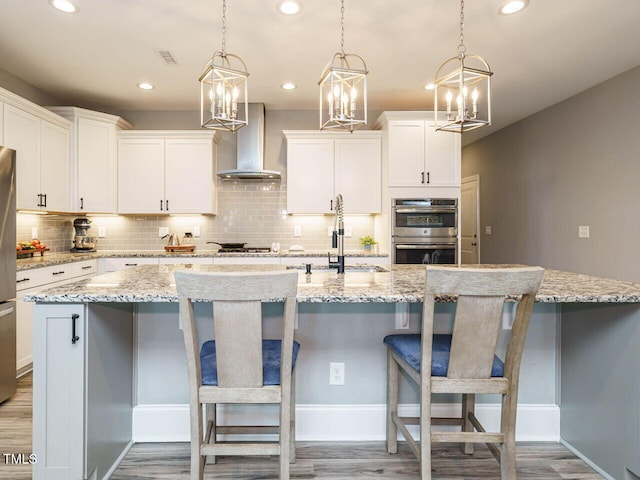 kitchen featuring wall chimney exhaust hood, a sink, tasteful backsplash, appliances with stainless steel finishes, and a kitchen island with sink