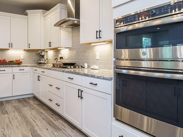 kitchen featuring wall chimney exhaust hood, stainless steel appliances, white cabinetry, and tasteful backsplash