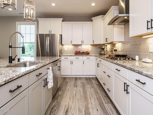 kitchen with wall chimney range hood, stainless steel appliances, a sink, white cabinets, and recessed lighting