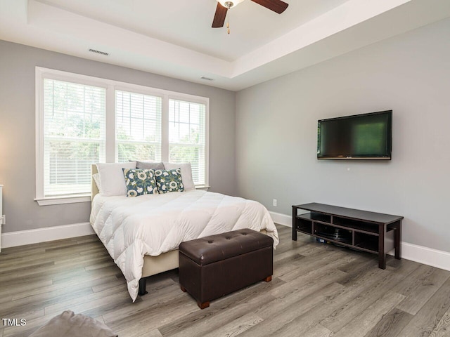 bedroom featuring baseboards, light wood-style floors, and a raised ceiling