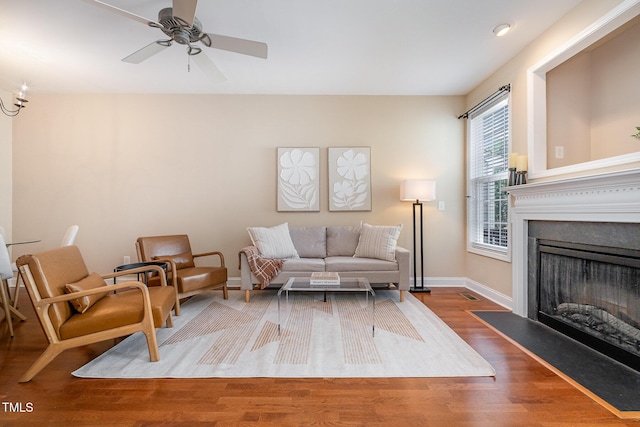 living room with wood finished floors, baseboards, ceiling fan, and a fireplace with flush hearth