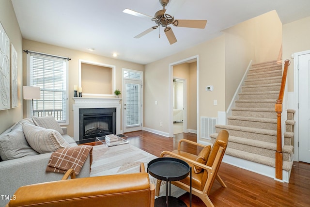 living area featuring wood finished floors, stairway, ceiling fan, a fireplace, and baseboards